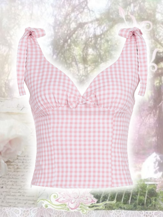 Pink gingham top with bow straps hanging against a blurred natural background