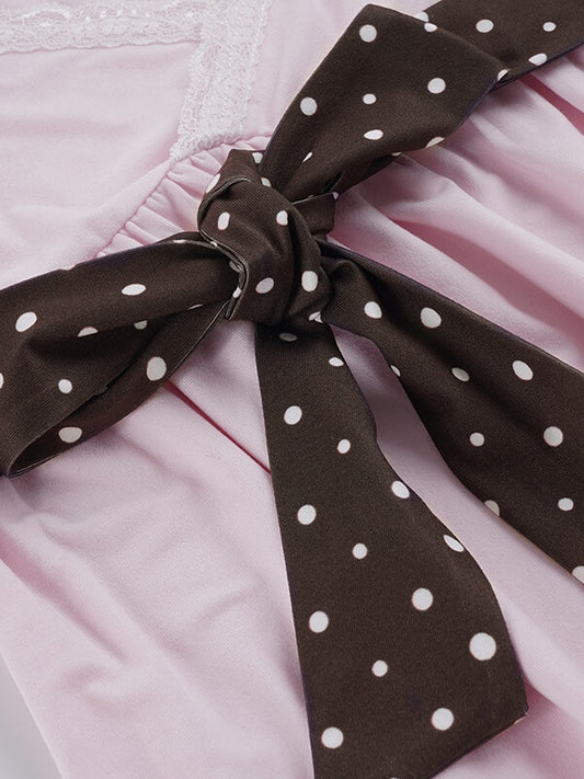 Brown polka dot ribbon tied into a bow on a pink background